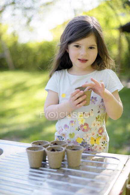 Jolie fille planter des graines dans de petits pots sur la table à la cour — Photo de stock