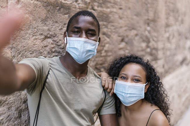 Молодая пара в масках, делая селфи у стены — стоковое фото