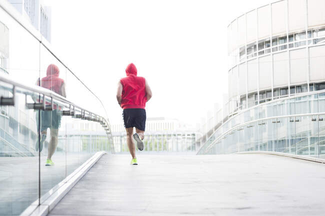 Rückansicht junger Mann joggt auf Fußgängerbrücke in der Stadt — Stockfoto