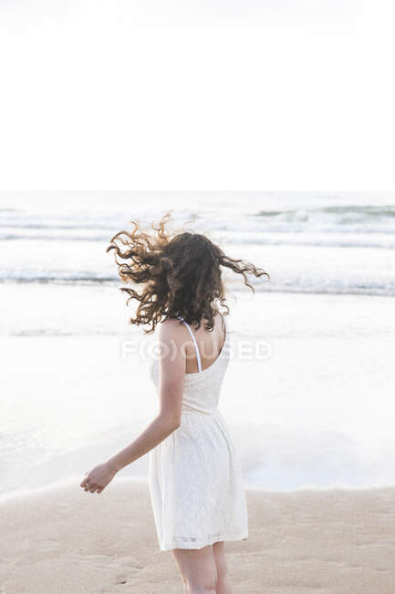 Молодая женщина в белом платье стоит на пляже против ясного неба — стоковое фото