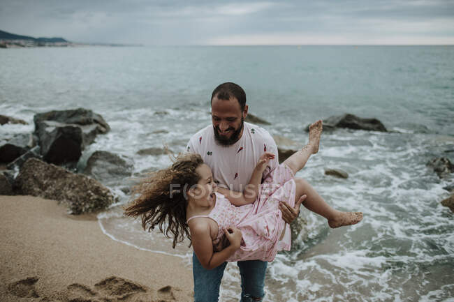 Père souriant portant fille à la plage — Photo de stock