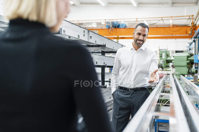 Homme d'affaires souriant et femme aux tiges de métal dans le hall d'usine — Photo de stock