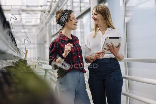 Smiling gardener and businesswoman with tablet in greenhouse of a gardening shop — Stock Photo