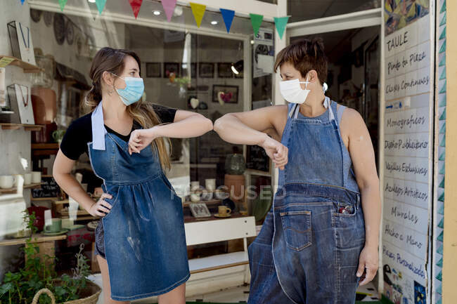 Colleghe donne che indossano maschere dando gomito urto mentre in piedi contro officina — Foto stock