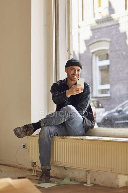 Человек ремонт магазин местоположение, сидя на подоконнике, используя смартфон — стоковое фото