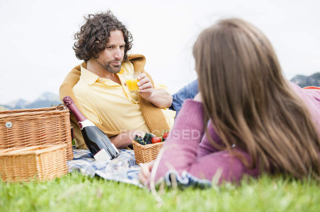 Handsome man drinking juice while reclining and looking at woman during picnic — Stock Photo