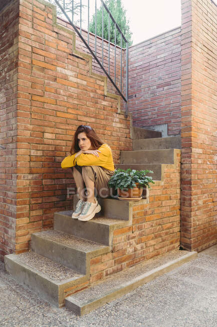 Sad thoughtful young woman sitting on steps by brick wall — Stock Photo