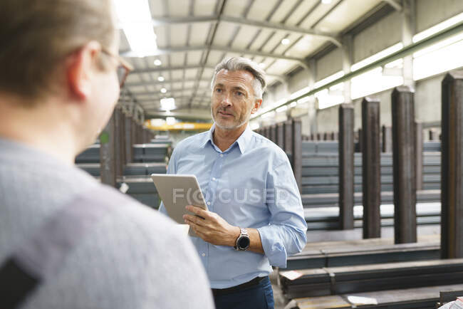 Бізнесмен з планшетом розмовляє зі співробітником на заводі — стокове фото