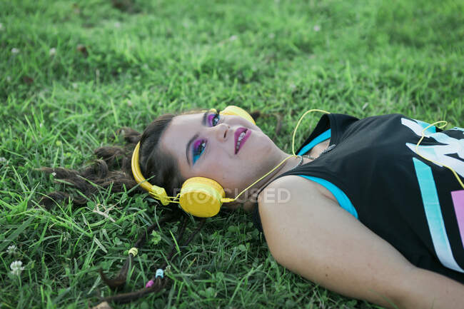 Menina adolescente com síndrome de down usando 8s maquiagem colorida e ouvir música com fones de ouvido amarelos — Fotografia de Stock