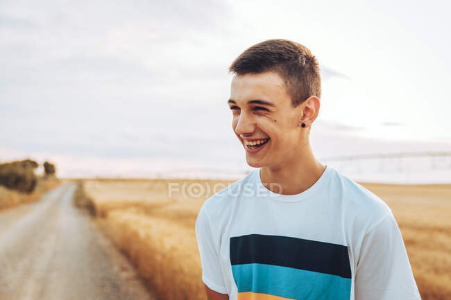 Allegro ragazzo adolescente che distoglie lo sguardo mentre si trova contro il paesaggio durante il tramonto — Foto stock