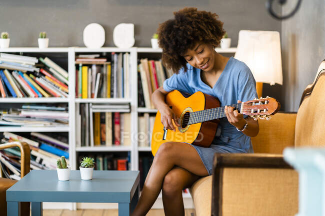 Счастливая женщина играет на гитаре, сидя на диване в кафе — стоковое фото