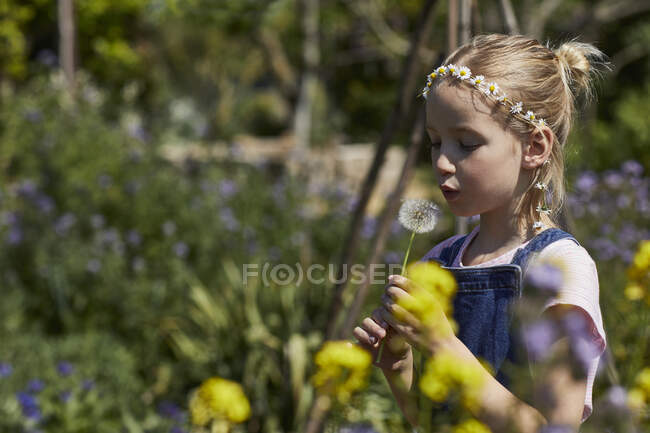 Menina no jardim de colocação usando guirlanda margarida soprando uma bola de sopro — Fotografia de Stock