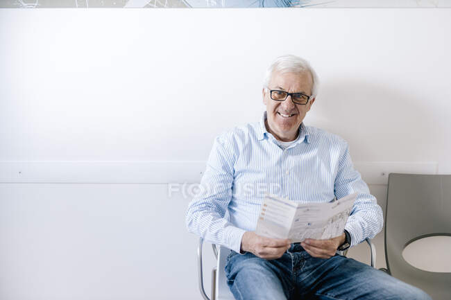 Uomo anziano seduto in sala d'attesa dello studio medico, volantino di lettura — Foto stock