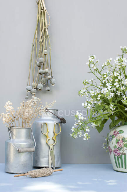Brotes de amapola secos, botes de leche, cuerdas, tijeras y flores en flor - foto de stock