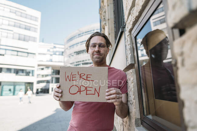 Shopkeeper sosteniendo cartón con anuncio de apertura en la ciudad - foto de stock