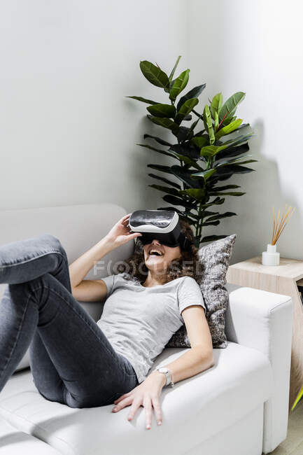 Jovem deitada no sofá em casa usando óculos de realidade virtual — Fotografia de Stock
