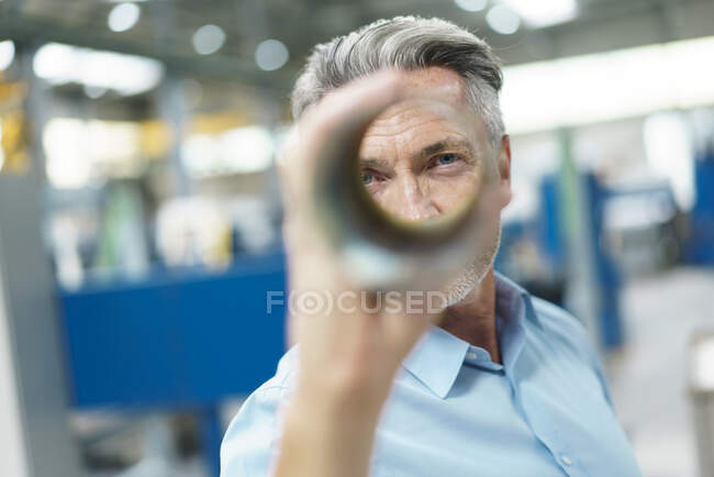 Businessman holding steel pipe in a factory — Stock Photo
