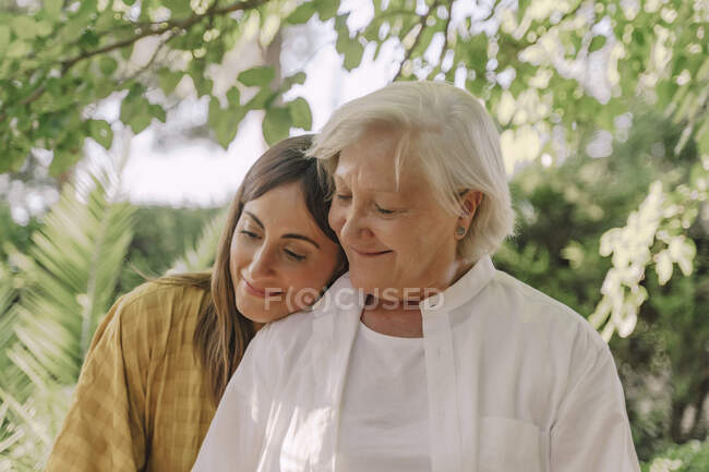 Close-up of smiling daughter embracing mother in yard — Stock Photo