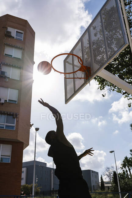 Молодий чоловік кидає баскетбол проти сонця. — стокове фото