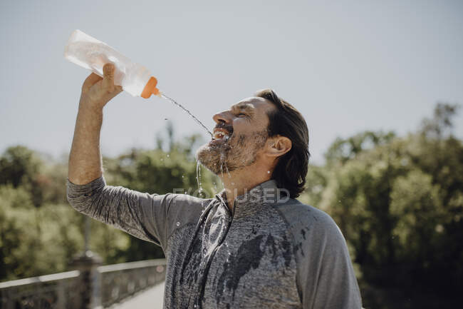 Крупный план взрослого мужчины, пьющего воду, стоя перед чистым небом в парке — стоковое фото
