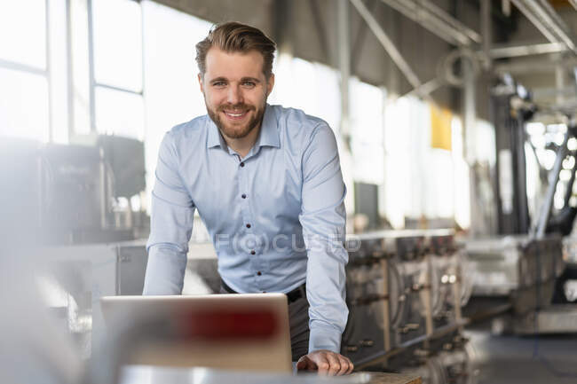Портрет улыбающегося молодого бизнесмена с ноутбуком на заводе — стоковое фото
