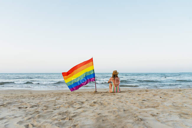Marure femme assis sur la plage avec gay pride drapeau — Photo de stock