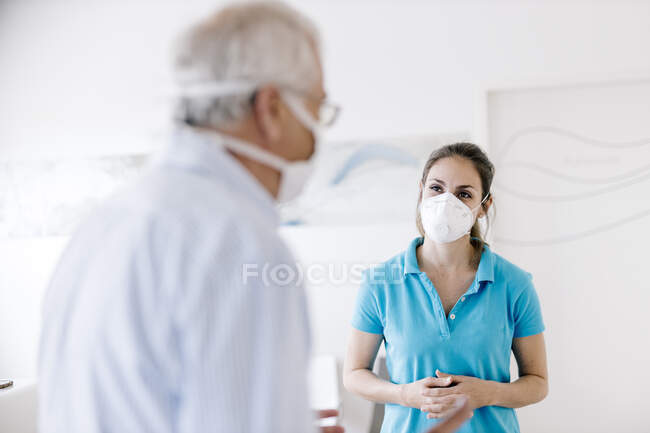 Uomo anziano che incontra il suo fisioterapista femminile alla reception, indossando maschere per il viso — Foto stock