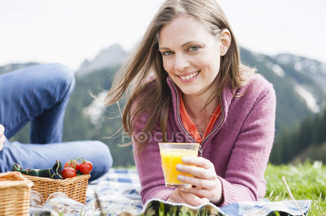 Portrait de femme souriante tenant du jus tout en étant couché par l'homme pendant le pique-nique — Photo de stock