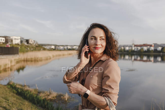 Красивая деловая женщина смотрит в сторону, используя смартфон на берегу озера — стоковое фото