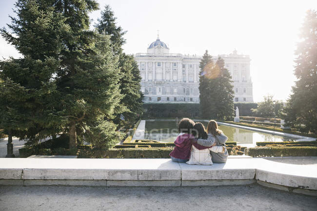 Multi-ethnic female friends embracing while looking at Madrid Royal Palace in park, Spain — Stock Photo