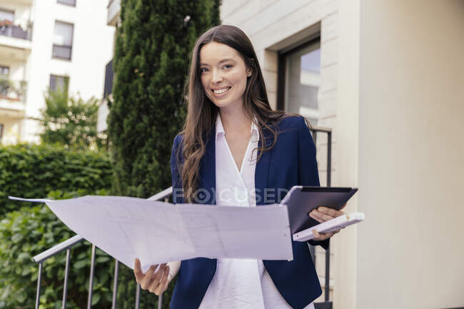 Portrait of smiling woman with digital tablet and face mask in hand outside a house — Stock Photo