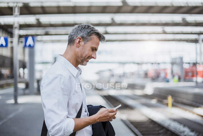 Businessman using smart phone while standing at railroad station platform — Stock Photo