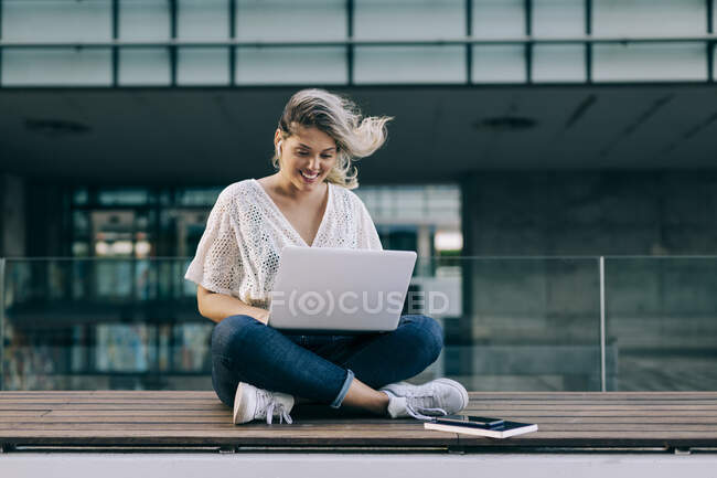 Empresária trabalhando no laptop enquanto sentado contra prédio de escritórios — Fotografia de Stock