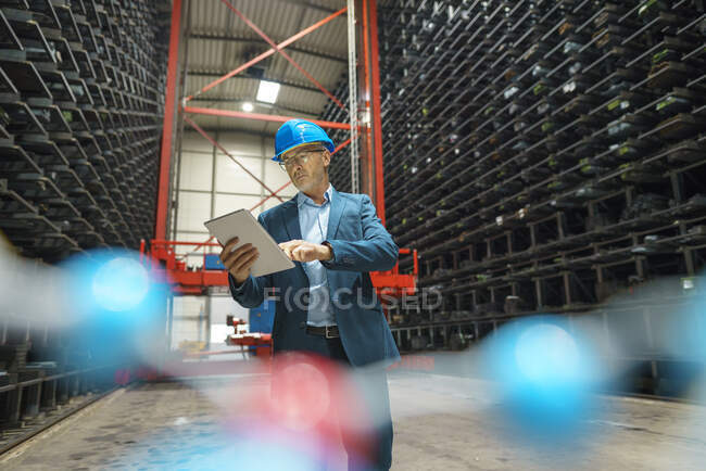 Mature businessman using tablet in a high rack warehouse of a factory — Stock Photo