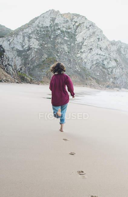Mujer joven dejando huellas mientras corre en Ursa Beach, Región de Lisboa, Portugal - foto de stock