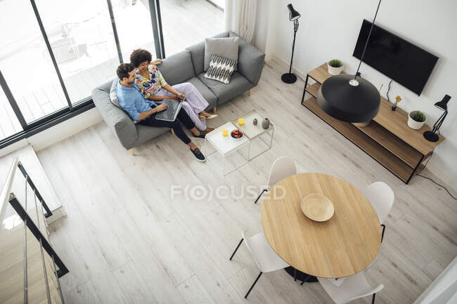 Multi-ethnic couple using laptop while sitting on sofa in living room of modern penthouse — Stock Photo