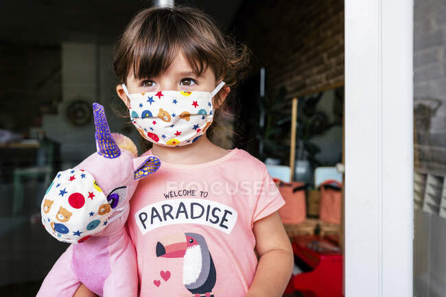 Retrato de chica con una máscara de colores y un juguete suave unicornio - foto de stock