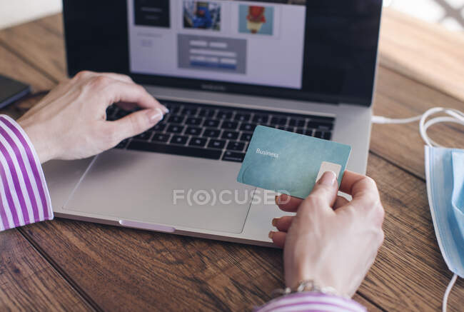 Mãos cortadas de empresária segurando cartão de crédito fazendo compras on-line sobre laptop no escritório — Fotografia de Stock