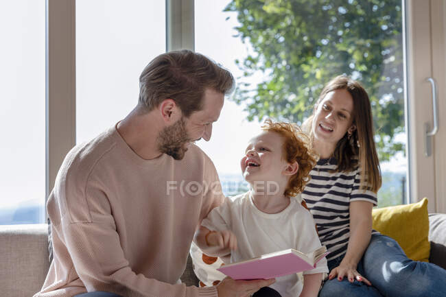 Lächelnder Junge schaut Vater an, während er bei Mutter im Wohnzimmer sitzt — Stockfoto