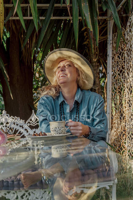 Porträt einer Seniorin, die auf einer Gartenbank sitzt und es sich bei Tee und Keksen gemütlich macht — Stockfoto