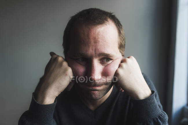 Primer plano del triste hombre adulto medio con la cabeza en las manos contra la pared en casa - foto de stock