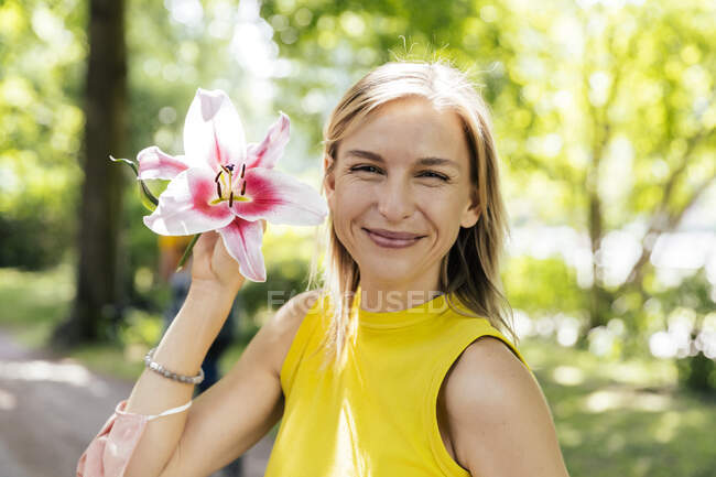 Retrato de una mujer sonriente en la naturaleza sosteniendo una flor de lirio - foto de stock