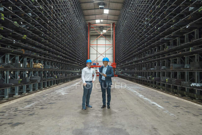 Dos hombres de negocios que tienen una reunión en un almacén de alto rack de una fábrica - foto de stock