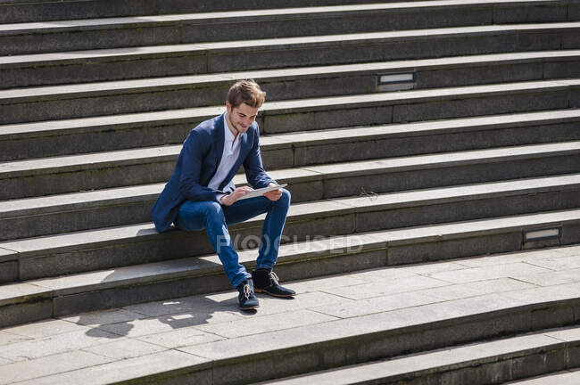 Jovem empresário sentado nas escadas usando tablet — Fotografia de Stock