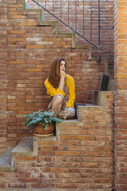 Скучная задумчивая женщина с ноутбуком и смартфоном сидит на ступеньках — стоковое фото