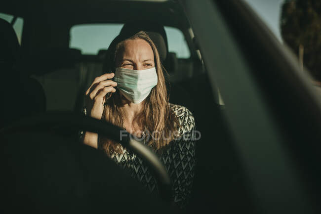 Mittlere erwachsene Frau mit Schutzmaske nutzt Smartphone im Auto — Stockfoto