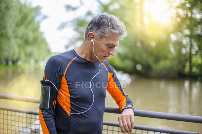 Active senior man looking at smart watch by railing at park — Stock Photo