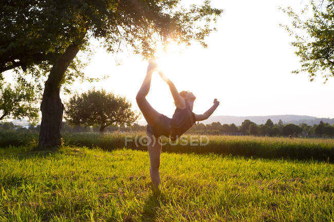 Девочка-подросток, занимающаяся йогой на травянистом поле на закате — стоковое фото