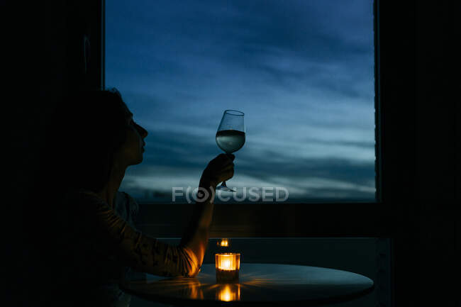 Silhouette birthday woman sitting with wineglass by window at home during sunset — Stock Photo