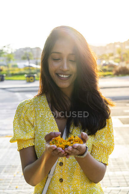 Woman smiling while holding flowers in cupped hands in city during summer — Stock Photo